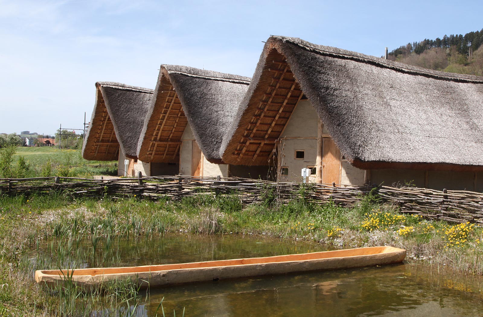 Pfahlbauhäuser und Teich mit Einbaum
